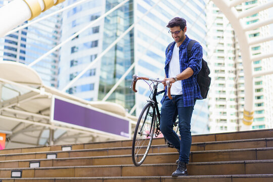 Asian man walking bicycle in city, commuting to work for fitness and eco-friendly lifestyle.