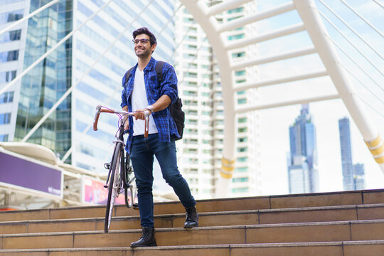 Asian man walking bicycle in city, commuting to work for fitness and eco-friendly lifestyle.
