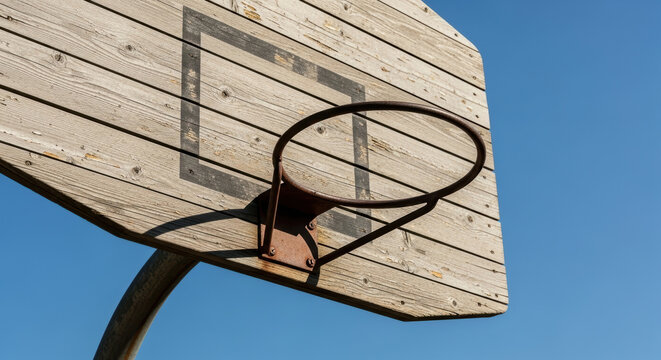 Weathered outdoor wooden basketball hoop with metal rim mounted against clear blue sky, representing urban sport nostalgia and recreational activity, dry sunny day - Powered by Adobe