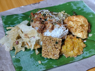 Nasi pecel or sego pecel is a typical Javanese Indonesian rice dish served with pecel sauce, which can be added with vegetables, peyek, eggs, tempeh and other side dishes. With basic ingredients of ba