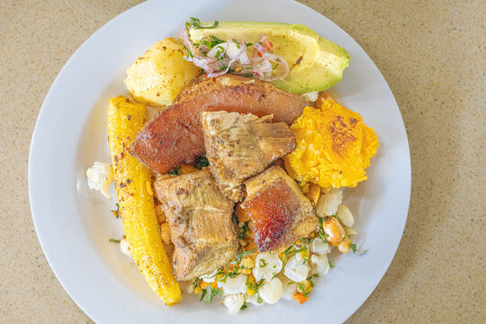Ecuadorian fritada or Ecuadorian fried pork served with mote, fried plantain, fried pork, fresh salad, avocado, potato, and toasted corn on a colorful plate. A traditional Andean feast full of flavor.