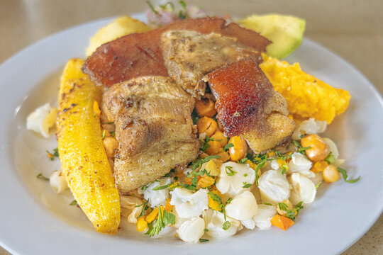 Ecuadorian fritada or Ecuadorian fried pork served with mote, fried plantain, fried pork, fresh salad, avocado, potato, and toasted corn on a colorful plate. A traditional Andean feast full of flavor.