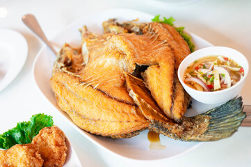 Crispy fried fish with fish sauce served on a white plate, accompanied by spicy mango salad and seafood dipping sauce. Classic Thai dish combining crispy texture and bold flavors.