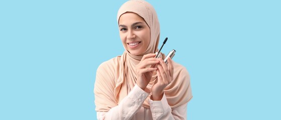 Pretty young Muslim woman with mascara on light blue background
