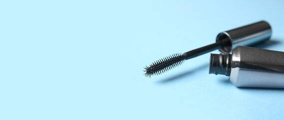 Black mascara on light blue background with space for text, closeup