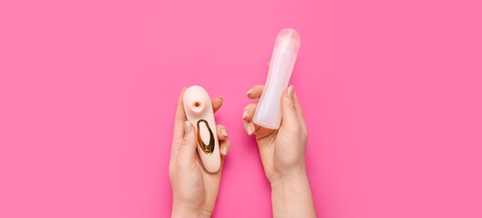 Woman's hands holding clitoral suction vibrator and and bottle of lubricant on pink background, top view
