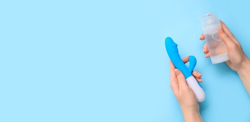 Woman's hands holding rabbit vibrator and bottle of lubricant on blue background with space for...