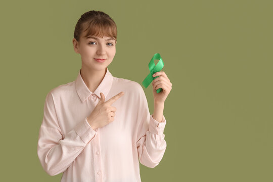 Young businesswoman pointing at green ribbon on color background. Glaucoma awareness month