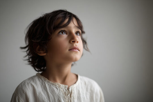 young boy gazes upwards with despair in his eyes against clean solid color background