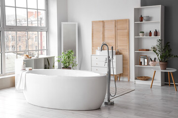 White bathtub in interior of spacious bathroom with panoramic windows