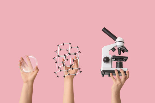 Female hands holding microscope with molecular model and Petri dish on pink background. Chemistry lesson concept