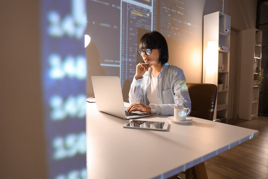 Young female programmer working with laptop in office at night - Powered by Adobe