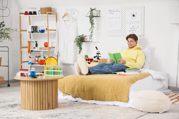 Male student with book studying Chemistry in bedroom