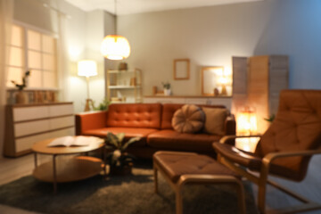 Interior of living room with brown sofa, armchair and glowing lamps in evening