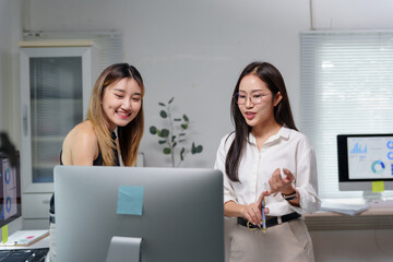 Two Asian businesswomen are discussing work while looking at a computer screen in a modern office