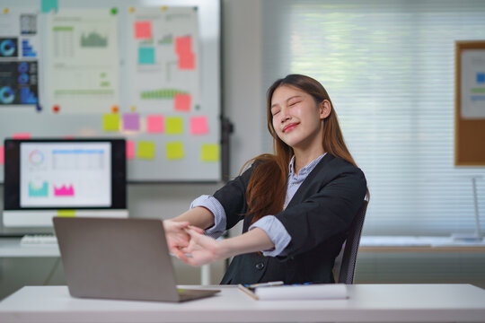 Asian businesswoman stretching her arms at workplace after working on a laptop computer in the office