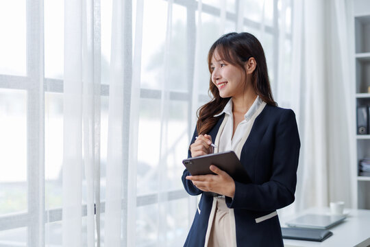 Businesswoman using a tablet and stylus, contemplating ideas near a bright window in a modern office, embodies professionalism and innovation - Powered by Adobe