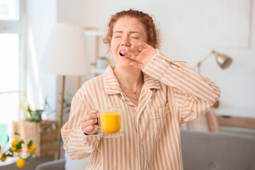Fototapeta premium Sleepy young redhead woman in pajamas with turmeric drink at home