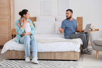 Displeased man and his wife with little baby in bedroom