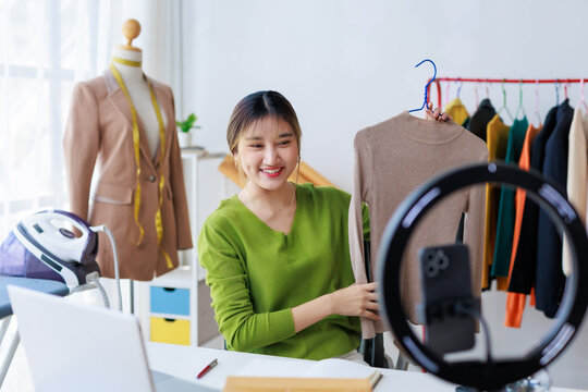 Asian fashion designer presenting new clothes during online streaming video blog from her workshop