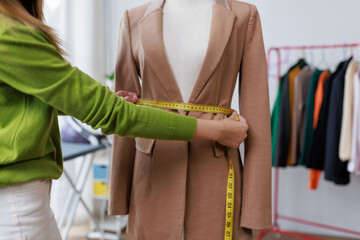 Fashion designer taking measurements of a suit jacket on a mannequin using a tape measure in her workshop