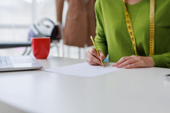 Fashion designer sketching clothing ideas in a bright, modern workshop, surrounded by tools of creativity and inspiration