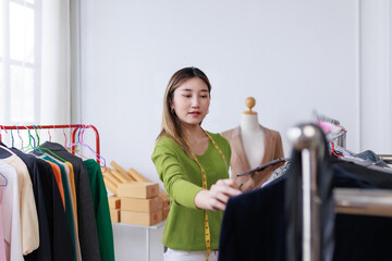 Asian female fashion designer using digital tablet for managing clothes inventory in her workshop or store