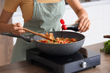 Young woman with soy sauce frying rice and vegetables in kitchen, closeup