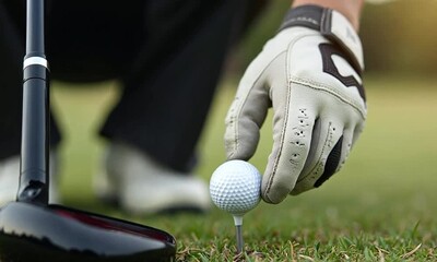Golfer placing a golf ball on a tee with a golf club on the green grass course - Powered by Adobe
