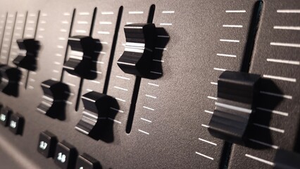 Close-up view of fader sliders and control buttons on a professional lighting control panel.