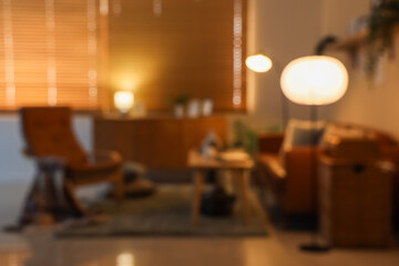 Blurred view of dark living room with glowing lamps, sofa and armchair at night