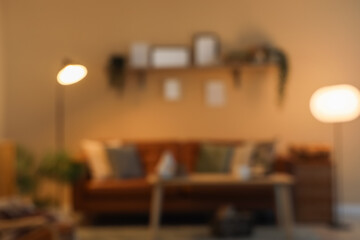 Blurred view of dark living room with glowing lamps, sofa and shelf at night