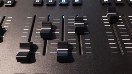 Close-up view of fader sliders and control buttons on a professional lighting control panel.