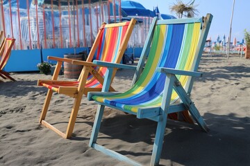 Beach chairs on the beach. The chairs are colorful. The background is blue. The place is for relaxing.