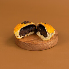 A halved chocolate-filled bakpia with golden crust placed on a small round wooden board, showing its rich dark filling against a warm brown background.