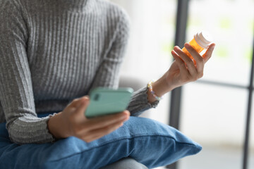 Young Asian Woman Searching Medicine Info on Smartphone with Bottled Drug at Home for Healthcare Wellness and Lifestyle