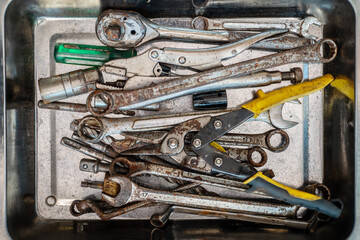 Flat lay rusty and worn wrenches and tools,Pliers screwdriver wrench rusted iron metal tools in stainless steel tray at garage