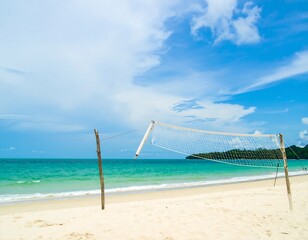 Beach volleyball net on a sandy shore under a partly cloudy sky