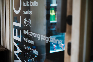 Multilingual welcome sign decal  on the transparent glass door of a tourist spot kiosk selling cold beverages with a refrigerator seen on the background