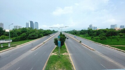 Elevated urban road view with green median, modern buildings, and distant misty mountains