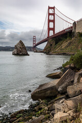 
Golden Gate Bridge view from rocky shoreline on cloudy day.