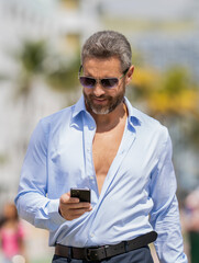Fototapeta premium Business communication. Casual business man chatting on phone outdoor. Businessman using phone. Man relax on bench with phone. Hispanic business man with phone. Modern businessman communication