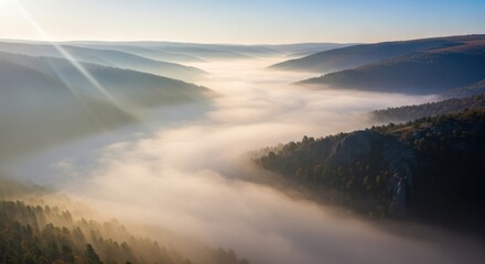 Golden sunbeams pierce a river of morning fog flowing through a serene, layered mountain valley.