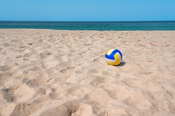 Obraz premium Colorful volleyball on sandy beach with calm sea and sunny sky