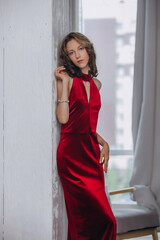 Fototapeta premium The model is a young beautiful girl in a red long dress in the interior