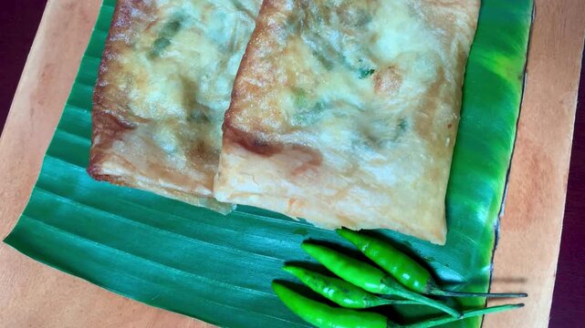  Crispy Indonesian martabak telor served with fresh green chilies on banana leaf, 4K detail shot. Perfect for food, culinary, and street snack projects.