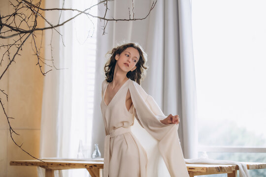 The model is a young beautiful girl in a flowing dress in a cozy interior in warm colors