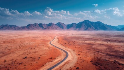 Naklejka premium A winding road snakes through a vast, arid landscape, framed by distant mountains. A vibrant palette of warm earth tones and a hazy sky complete the scene