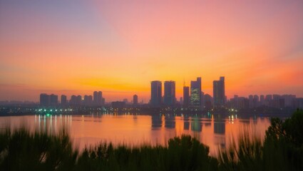 Fototapeta premium City skyline at sunset reflected in calm water with silhouetted trees