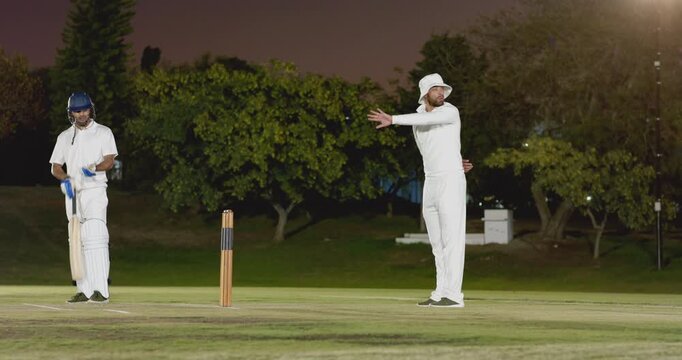 Umpire raising arm to signal bowler, bowler running in, bowling ball on pitch, batsman leaving ball